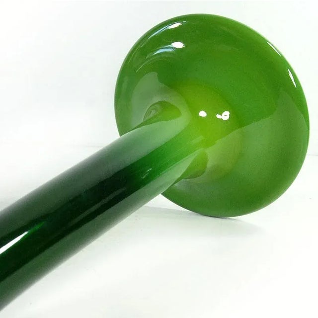 A beautiful, tall, and slender single-flower vase made of hand-formed glass in a deep, saturated green. The glass smoothly...