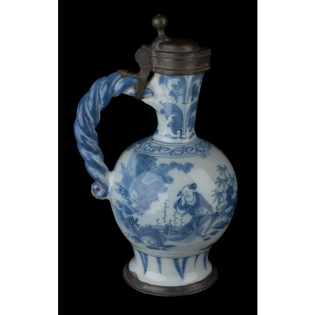 The blue and white wine jug has a round body standing on a wide, spreading foot, and a slightly conical neck with pouring...