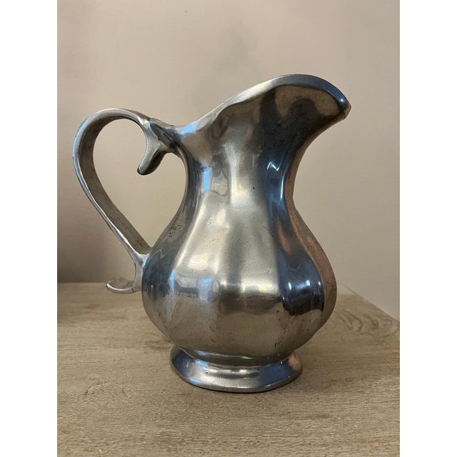 This vintage Italian pewter pitcher features a bulbous body, a gracefully curved handle, and a raised circular footed...