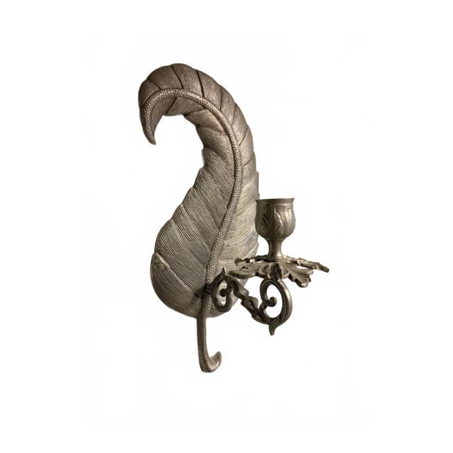 This vintage wall-mounted candle holder features an intricately detailed metal leaf design with a silver finish. The piece...