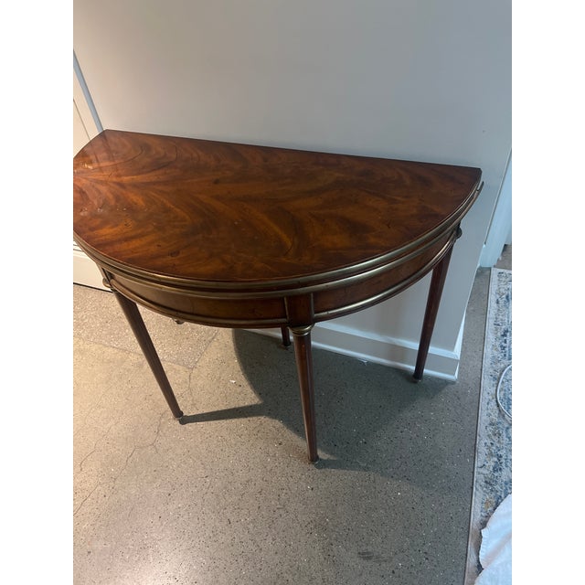 mahogany demi lune flip top console game table. On fluted legs with gilt bronze trim. Tooled leather top. Late 20th...