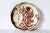 Whimsical brown and cream colored pottery plate with a female, mushroom and floral motif. Signed by artist. Minor age wear.