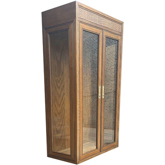 A tall wooden display cabinet with a warm natural finish and two glass-paneled doors. The clean rectangular shape and...