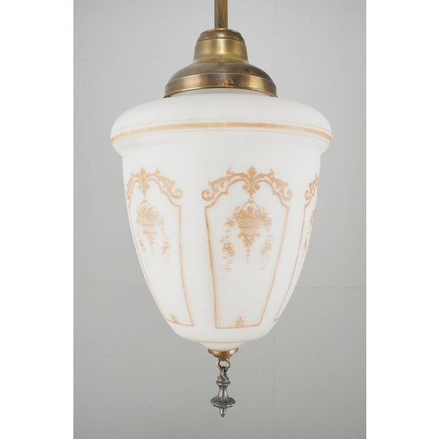 Neoclassical style pendant light with a stenciled milk glass shade, brass pole fitter and a steel ornate finial. This...