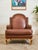 A stately leather bergère-style armchair featuring a gracefully arched back, rolled arms, and hand-applied brass nailhead...