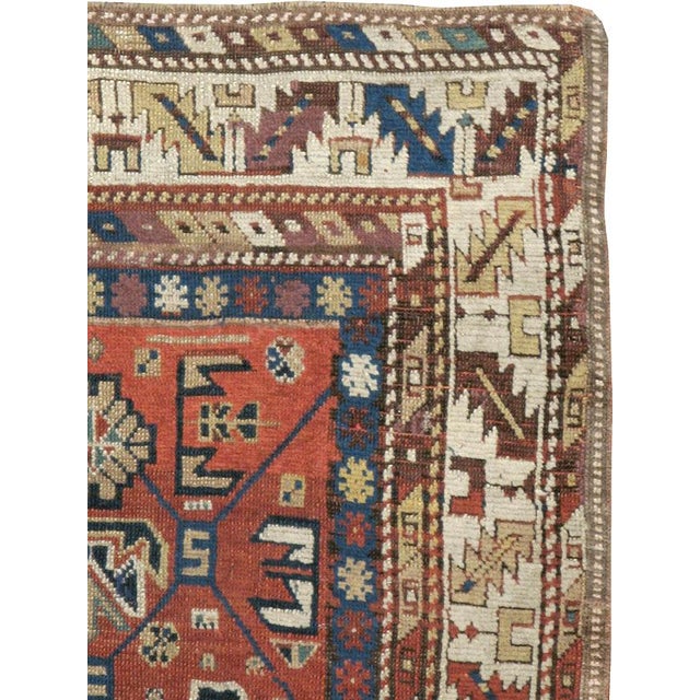 An antique Caucasian Kazak throw rug. The red field is divided by a subtle trellis with geometric palmettes and leaves in...