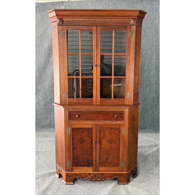 This antique bench-made burled walnut corner cabinet showcases rich figuring, glass-paneled upper doors for display, and a...