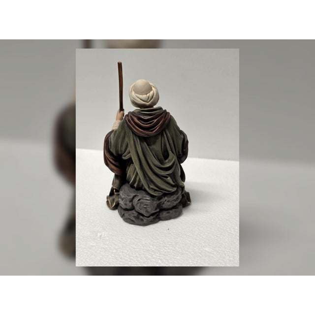 This Italian Baroque style shepherd figurine represents a seated pastoral figure in a moment of quiet rest, holding a...