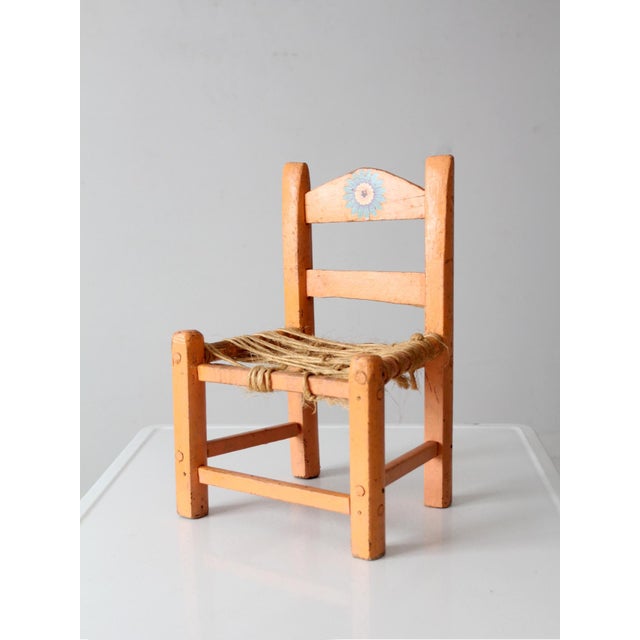 A vintage Mexican child’s chair finished in a warm peach tone with a floral stencil along the back crest and a woven fiber...