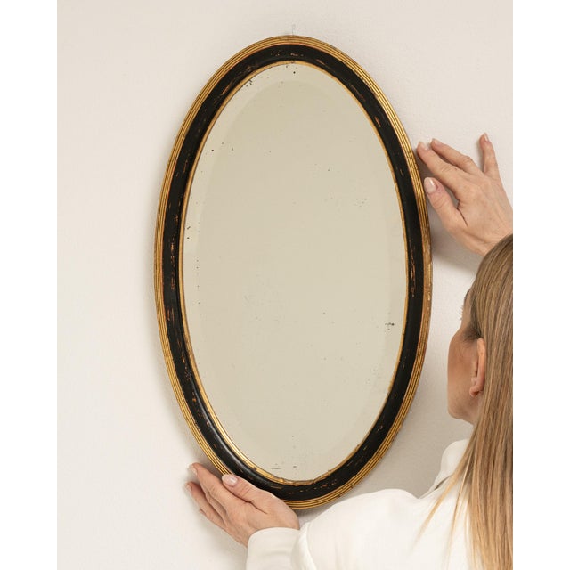 This mirror makes its impression through black frame with gold inner edge, oval. Dating to Early 20th Century and...