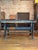 Rugged and weathered industrial table with heavy duty steel base and thick wooden top aged with a bluish-gray patina. Has...