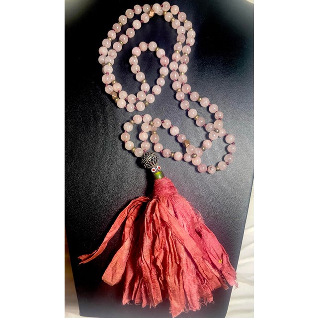 This mala-style necklace 32” long with 4.5” tassel drop, features a hand-knotted strand of soft pink rose quartz...