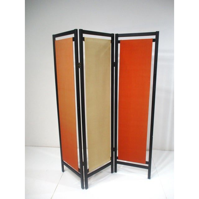 A three panel satin black wood framed room divider screen with colorful canvas inserts in orange and tan . Manufactured by...