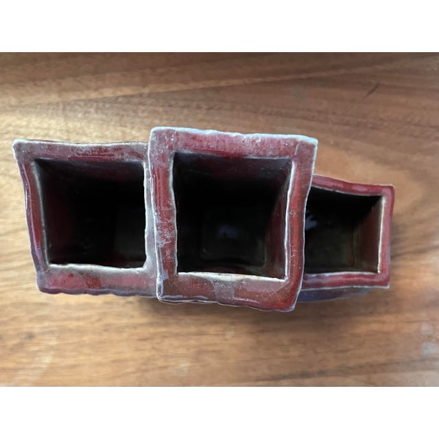 bold, sculptural vase with three compartments joined side by side. deep, glossy reddish brown glaze. accented with a...