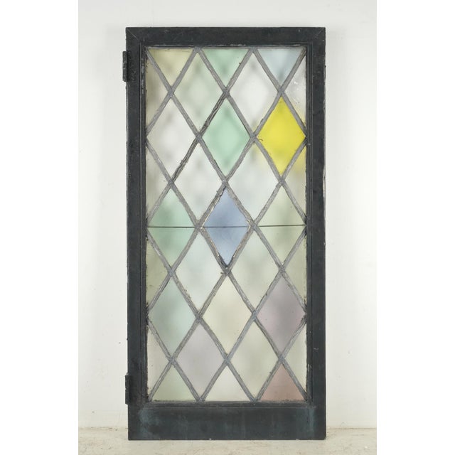 Tudor style casement stained glass window with a leaded diamond pattern in a pastel color scheme. The frame is made of...