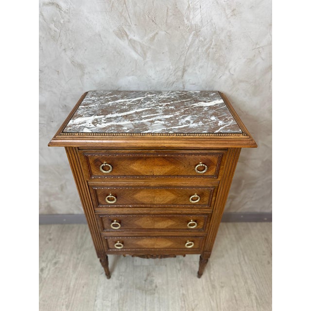 A charming Louis XVI style chest of drawers dating from the 1920s, crafted from walnut and topped with an elegant veined...