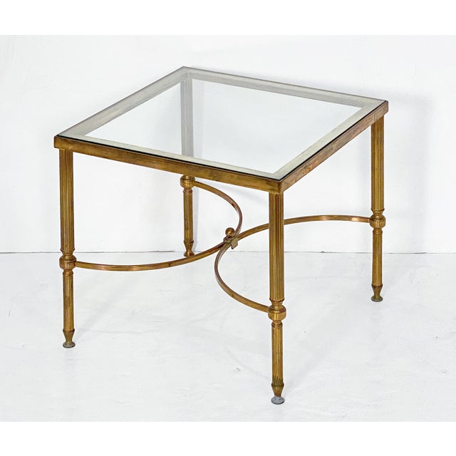 A French cocktail or low end table with Modern styling, featuring a square glass top set upon a brass frame of tapered,...