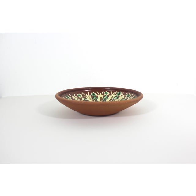 This is a vintage red clay ceramic pottery plate or bowl, hand-painted, showcasing traditional folk art. This is signed by...