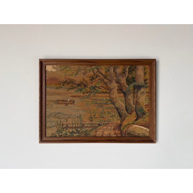 A charming vintage framed needlepoint textile depicting a peaceful lakeside landscape with trees, a small boat. Woven in...