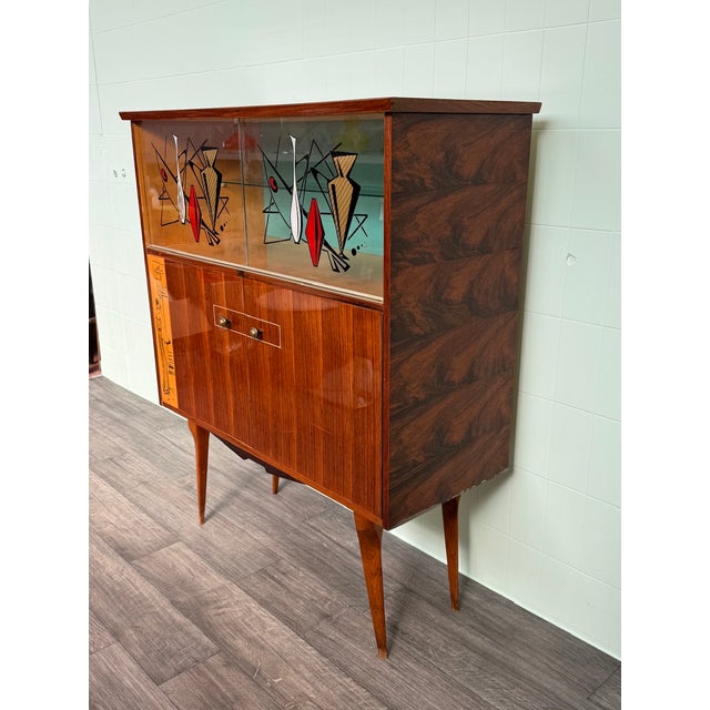 Vintage Italian cabinet with tall legs. Beautiful sliding glass doors with hand-painted decorations. The lower section is...