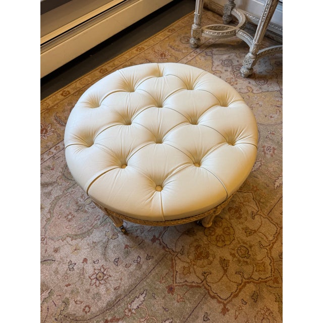 This is a vintage mid century French ivory leather tufted ottoman. It is Louis XVI style. It has a fluted leg on castors.