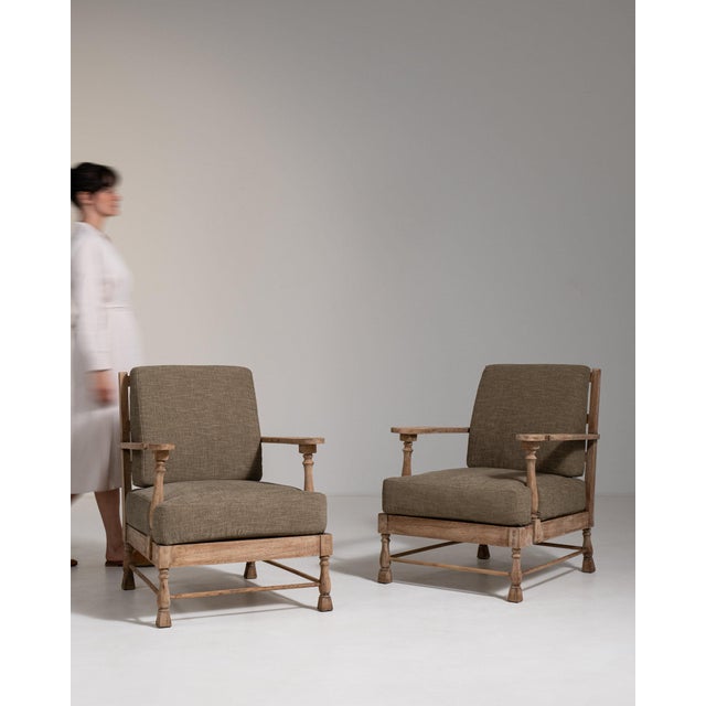 This piece presents as a pair of armchairs, distinguished by sage/olive upholstery, natural wood frame. The piece dates to...