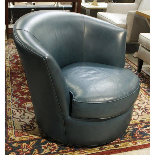 This swivel chair features smooth teal blue leather with a rounded barrel silhouette that wraps comfortably around the...