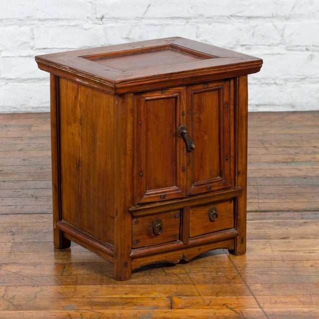 An antique Chinese elm wood bedside cabinet from the early 20th century with double doors, two drawers and brass hardware....