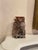 A hand-carved soapstone vase in mottled russet and grey tones, with natural veining and warm reddish and taupe variations...