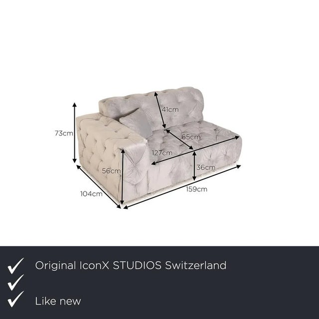 Iconx Studios' couch is covered with a gray velvet fabric and stands on black, inconspicuous feet. It is characterized by...