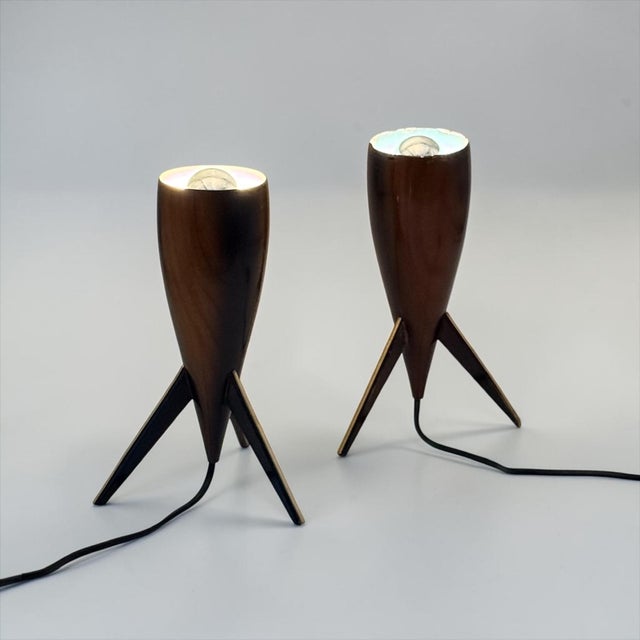 A pair of sculptural wooden tripod table lamps, dating approximately to the 1960s. their elongated, tapered wooden bodies...