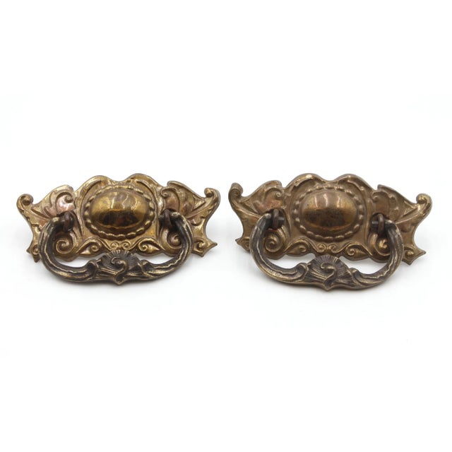 Victorian style dresser drawer pulls made of brass with a patina finish with a steel handle. The design includes floral...