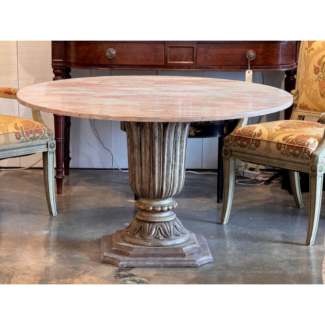 A round carved silverleaf pedestal table with a pink marble top. The urn-form base is fluted with acanthus leaf and beaded...