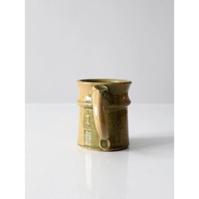 A vintage studio pottery mug, hand-crafted and signed by the artist, featuring a warm golden glaze reminiscent of...