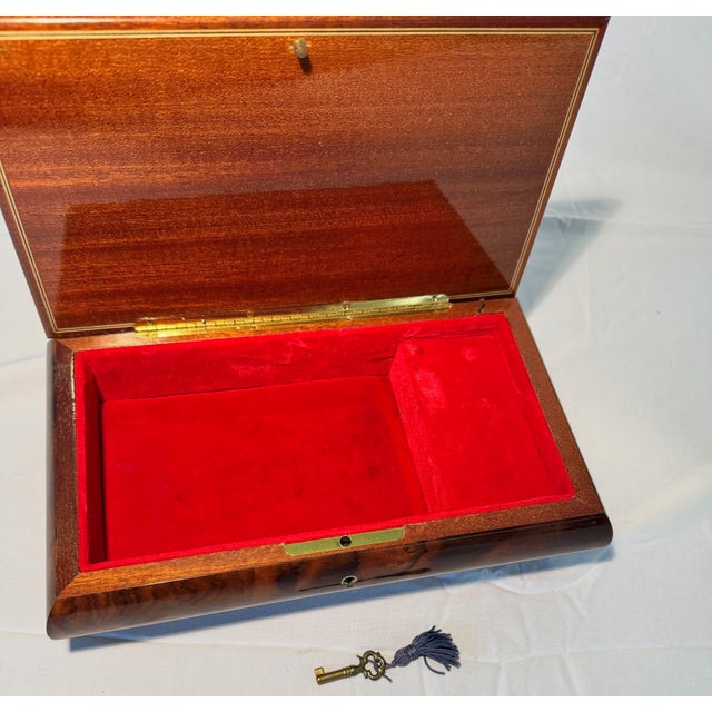 A nice wooden jewelry box with marquetry woodwork and a red velvet compartment inside. A sticker on the bottom states that...