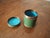 Green Chinese Cloisonné cylindrical box with subtle swirling copper decorations and a blue interior and underside.