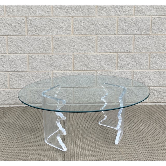 unique coffee table features a sculptural lucite base with a wavy design, supporting a sleek oval glass top