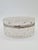 An elegant, oval-shaped box made of richly faceted pressed glass, with a decorative hinged lid and a metal frame. The...