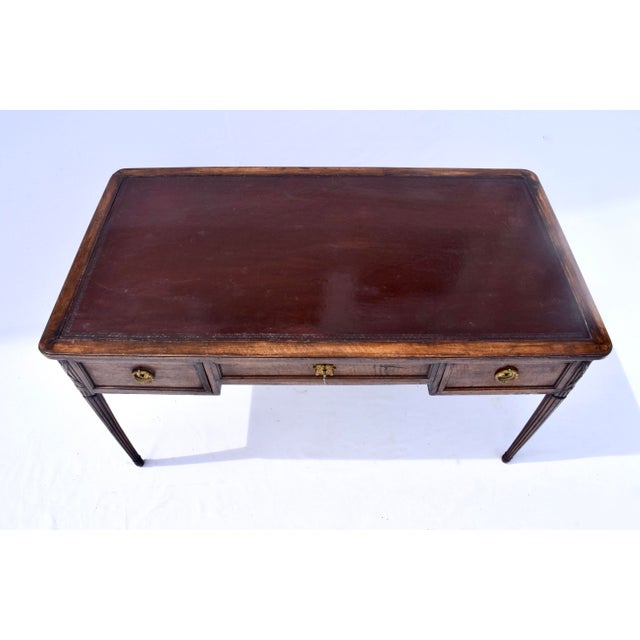 An early 20th c. Louis XVI style leather top desk with three drawers, original brasses and tapered reed legs; by Cassard...
