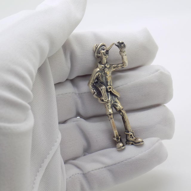 Enchanting and rich in narrative charm, this vintage silver figurine depicts Pinocchio heading off to school while holding...
