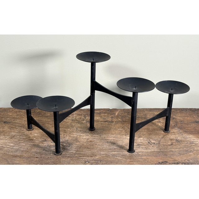 This black metal candle holder features a multi arm design with tiered disc platforms, each fitted with a center spike for...