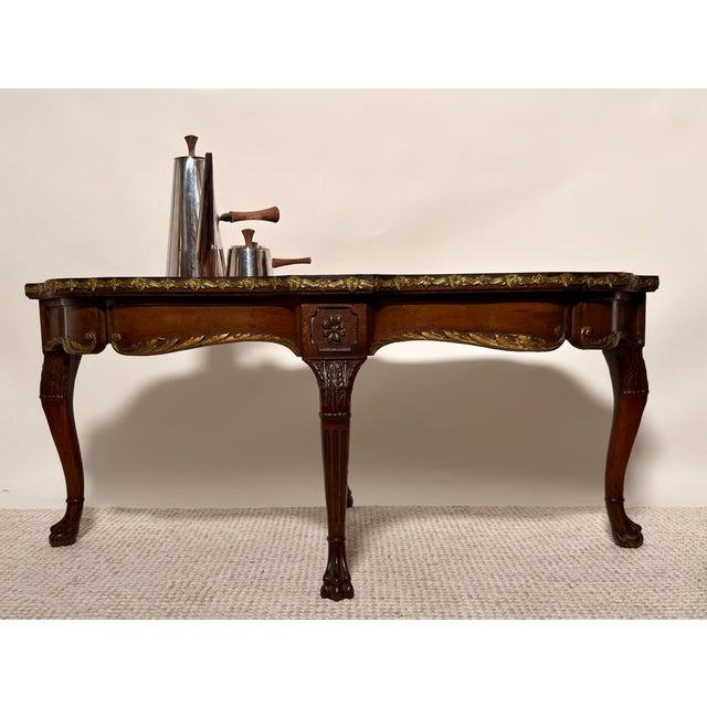 A refined Louis XV style cocktail table featuring a richly figured burl marquetry top framed by gilt ormolu trim. The...