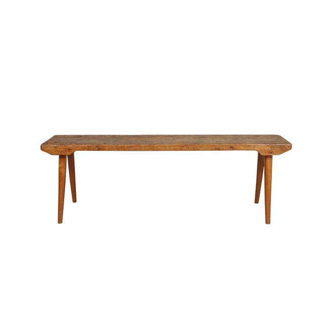A primitive solid wood bench, rich with patina, grain and fissures in the wood. Carved with four slightly splayed legs. We...