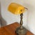 Brass and bronze-toned banker's desk lamp with an amber glass shade. Switch and outlet conveniently on base. Gives off a...