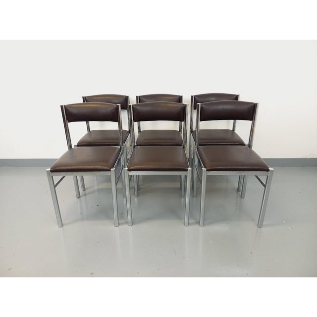 Six vintage chairs from the 1970s, with a chromed metal design, dark brown faux leather seats and backs, and a tubular...