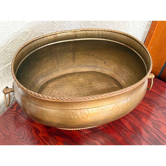 Large oval hammered brass cauldron planter with a rope twist rim and a matching rope foot. Large ring handles hang at each...