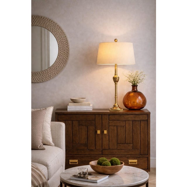 A tall, refined table lamp finished in a warm sunlit brass tone, newly styled with a 16” linen drum shade and oversized...