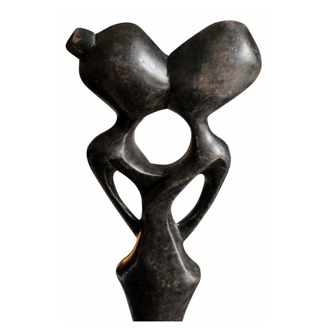 Hand-carved wood sculpture depicting an abstract couple in a unified, flowing form. The elongated figures and negative...