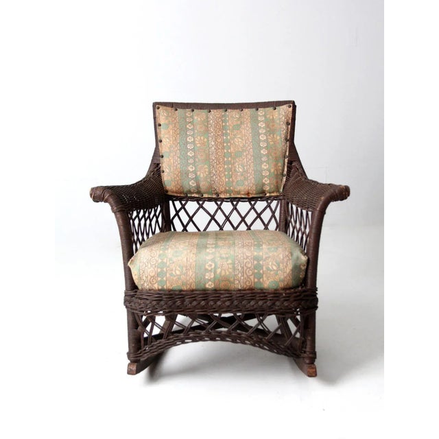 Here is an antique American wicker rocking chair circa late 19th century. The brown wicker rocker features a cushioned...