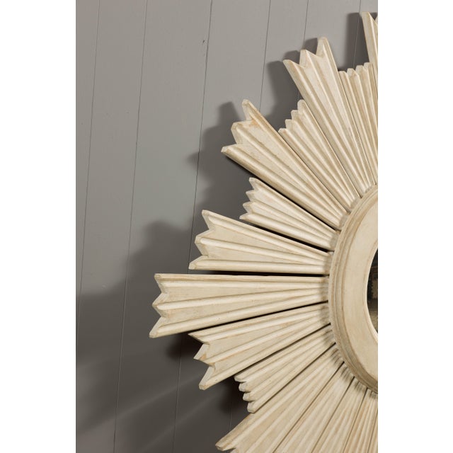 Modern painted wood sunburst mirror with light painted finish, small convex mirror and rays of alternating heights. This...